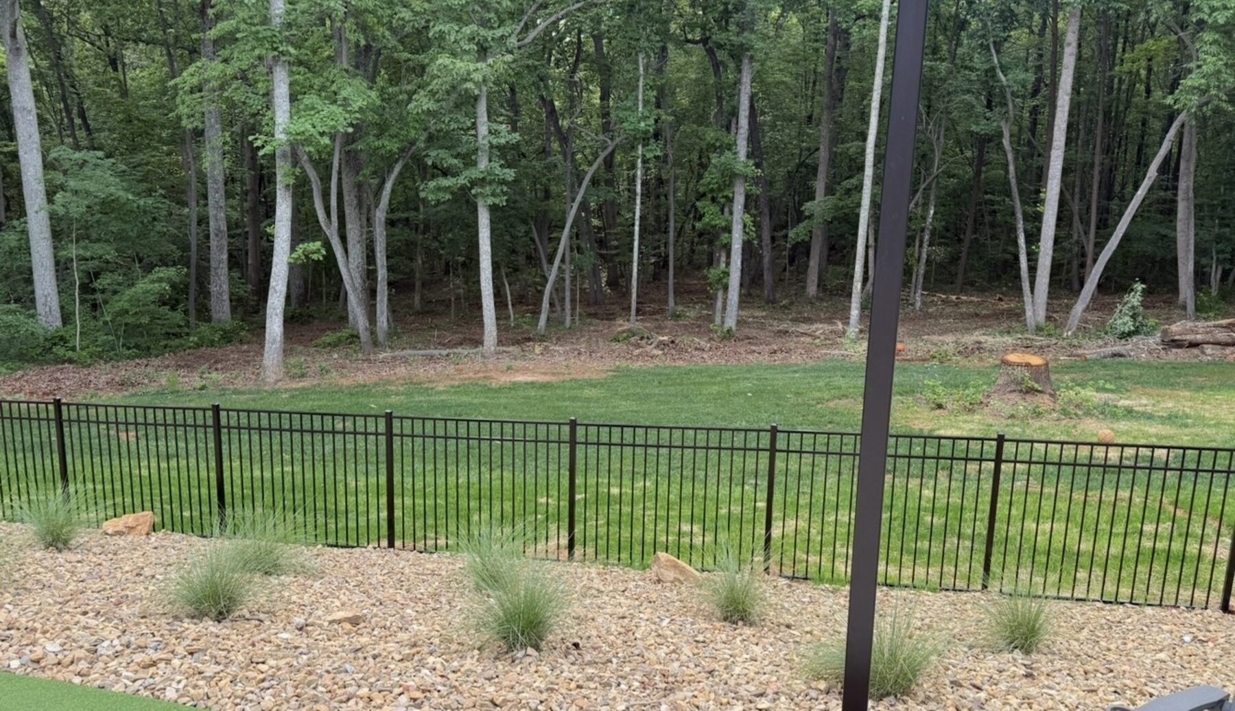 A finished yard with new lawn, a black fence and a gravel bed at the wood line